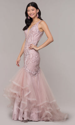 A woman wears the Embroidered V-Neck Mermaid Formal Prom Dress 8320, a sleeveless light pink gown with lace, tulle, and a deep V-neckline, as she smiles against a plain background.