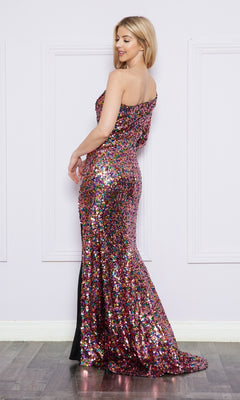 A woman poses sideways against a white paneled wall, elegantly wearing the One-Long-Sleeve Long Sequin Prom Dress 9022—an eye-catching, floor-length gown with multicolored sequins and an off-the-shoulder design.