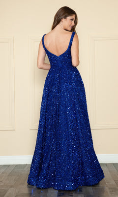 A woman faces away from the camera, wearing the Poly USA 9106 Velvet-Sequin Long A-Line Prom Gown in deep blue with a sleeveless design and V-back, standing against a beige wall.