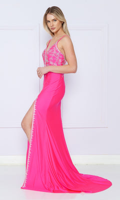 A woman in the Backless Long Jersey Prom Dress: Poly USA 9120, a bright pink gown featuring beads, a thigh-high slit, and an embellished bodice, stands against a light-colored wall.