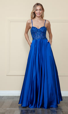 A woman wearing the Sheer-Corset Long Satin Prom Dress by Poly USA 9126 in royal blue, featuring thin straps, an embroidered corset bodice, and a flowing satin skirt, stands against a light-colored wall.