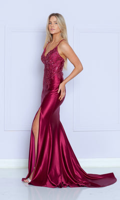 A woman stands against a light purple wall wearing the Embroidered-Lace-Bodice Long Jersey Prom Dress 9142, a sleeveless, floor-length gown with deep magenta lace, sequined bodice, and high slit.