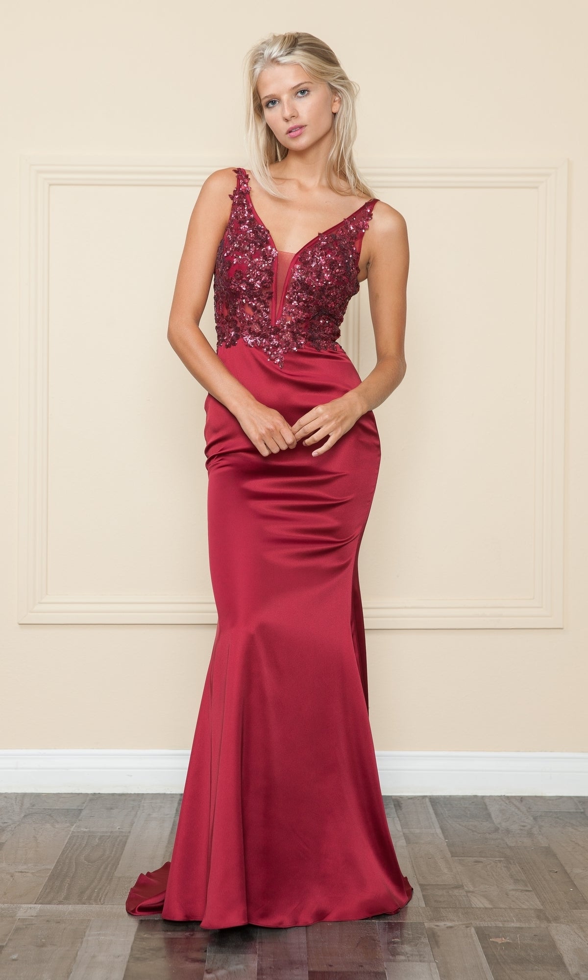 A woman wearing the Sequin-Bodice Long Satin Prom Dress 9162, a sleeveless red gown with a sequined bodice and satin skirt, stands against a beige wall and wooden floor.