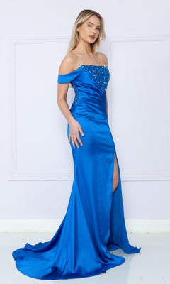 A woman stands against a light wall wearing the One-Shoulder Sequin-Bodice Long Prom Dress 9178, featuring a bright blue hue, sparkling sequins, bead embellishments, and a thigh-high slit.
