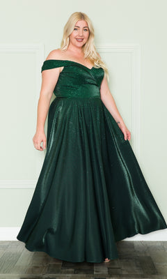 A woman wearing the Plus-Size Long Beaded Prom Dress with Pockets W1112, a floor-length dark green gown, stands against a pale wall, smiling with one arm slightly raised.