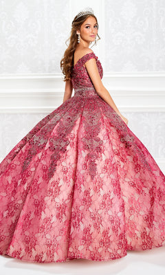 A young woman in a jeweled tiara wears the Princesa Lace Ball Gown Quinceañera Dress PR11921, featuring ornate beaded details and pink off-the-shoulder lace, posing against a white patterned wall.