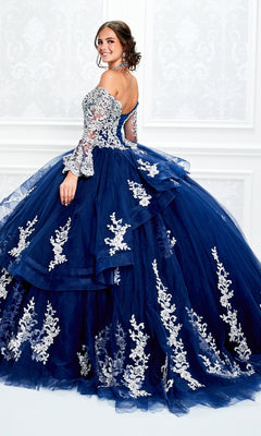 A woman poses in the Princesa Halter Ball Gown Quinceañera Dress PR11927, a blue gown with white floral embroidery, lace details, a halter neckline, and a full layered skirt.