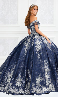 Young woman in a Princesa by Ariana Vara Quinceañera Dress PR12001, featuring off-the-shoulder design and silver floral embroidery, wearing a tiara in an ornate white room.