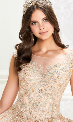 A woman poses indoors against a light background wearing the Princesa Traditional Lace Quinceañera Dress PR12002, featuring an ornate beaded bodice, sheer neckline, floral embroidery, and accessorized with a jeweled headpiece and earrings.