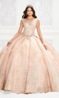A woman in the Princesa Traditional Lace Quinceañera Dress PR12002, a peach ball gown with silver embellishments and a tiara, stands before an ornate white backdrop.