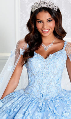 A woman in the Glow-in-the-Dark Princesa Quinceañera Dress PR12261, with a silver tiara and necklace, smiles at the camera against a light patterned background, highlighting the gown’s enchanting elegance.