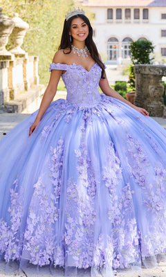 A woman wearing the Princesa Quinceañera Dress PR12263 with 3-D flowers and a tiara stands outdoors near stone steps and lush greenery.