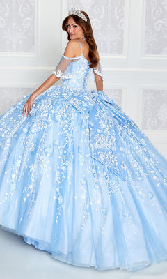 A woman wearing the Cold-Shoulder Princesa Quinceanera Dress PR12271 poses in front of a white paneled wall, looking over her shoulder.