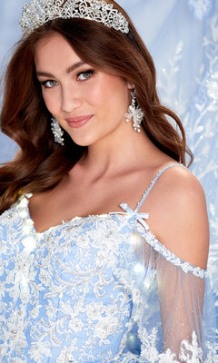 A woman smiles at the camera, wearing a silver tiara, sparkling earrings, and the Cold-Shoulder Princesa Quinceanera Dress PR12271 in light blue lace with sheer sleeves.