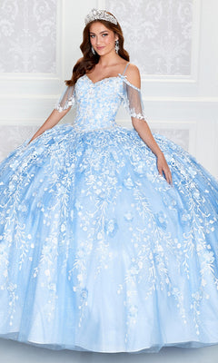 A woman wearing the Cold-Shoulder Princesa Quinceanera Dress PR12271, featuring light blue fabric, white floral embroidery, sheer sleeves, and a tiara, stands before a white decorative wall.