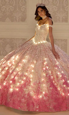 A woman poses indoors in the PR12275 Princesa Quinceañera Dress, a pink and white embroidered lace gown with built-in lights, accessorized with a tiara and choker necklace.
