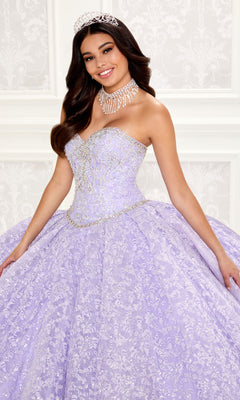 A young woman smiles at the camera indoors, wearing a jeweled tiara and the Strapless Quinceanera Dress: Princesa PR22022 in ornate lavender.
