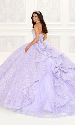 A woman in the Strapless Quinceanera Dress: Princesa PR22022, a lavender lace and ruffle gown, accessorized with a tiara and necklace, stands in an elegant white room, glancing over her shoulder.