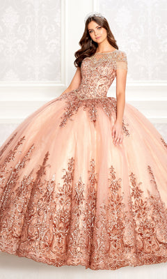 A woman wearing the Princesa PR22026 short-sleeve quinceanera dress with a beaded bodice and gold embroidery, paired with a tiara, stands before an ornate white background.