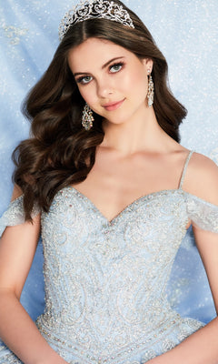A young woman in the Light Blue Quinceanera Dress: Princesa PR22032, featuring an off-shoulder design and lace appliques, poses with a sparkling silver tiara against a shimmery blue background.