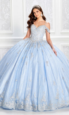 A woman in the Light Blue Quinceanera Dress: Princesa PR22032, with a corset bodice and silver accents, stands in an ornate white room as her tiara sparkles under the lights.