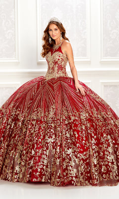A young woman in the Princesa PR22034 wine red quinceanera dress with gold embellishments and a jeweled tiara stands before a white patterned wall.