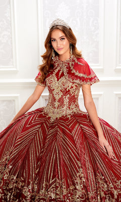 A young woman poses elegantly against a white, decorative wall in the Princesa PR22034 Wine Red Quinceanera Dress with gold embellishments and a matching removable bolero jacket.