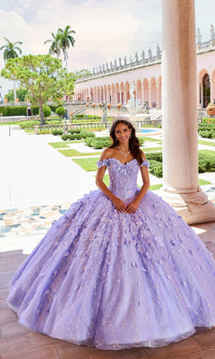 A young woman in the Flower Quince Dress: Princesa by Ariana Vara PR22036 stands under a column in a formal garden, with a historic building behind her, her lavender gown embellished with delicate floral accents.