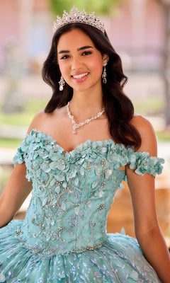 A young woman in the Flower Quince Dress: Princesa by Ariana Vara PR22036, a sparkly light blue ball gown, paired with a jeweled tiara and matching jewelry, smiles outdoors.