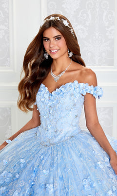 Young woman in the Flower Quince Dress: Princesa by Ariana Vara PR22036, a blue off-the-shoulder ball gown with floral details, accessorized with a tiara, necklace, and earrings, posing before a white patterned wall.