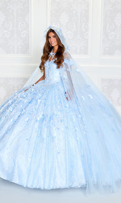 A young woman in the Flower Quince Dress: Princesa by Ariana Vara PR22036—with light blue floral details and a matching cape—stands before a white patterned wall, radiating dreamy elegance.
