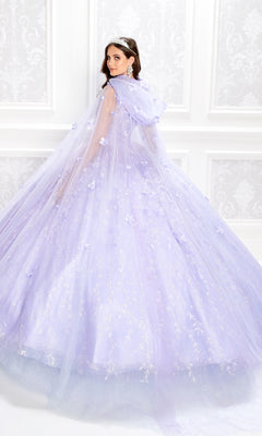 A woman wearing the Flower Quince Dress: Princesa by Ariana Vara PR22036, a light purple ballgown with a long cape, stands before a white ornate wall and looks over her shoulder.