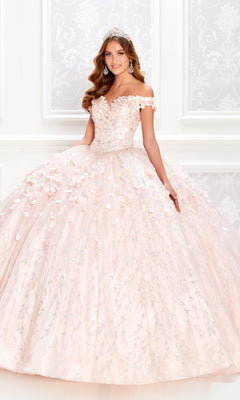 A young woman wearing the Flower Quince Dress: Princesa by Ariana Vara PR22036—a pink, off-the-shoulder ball gown with floral appliqués and a tiara—stands indoors before a patterned white wall.