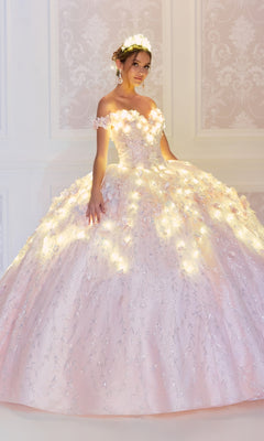 A young woman wears the sparkling, off-the-shoulder Flower Quince Dress: Princesa by Ariana Vara PR22036, featuring lights and floral details, as she stands in an elegant room with patterned wallpaper.