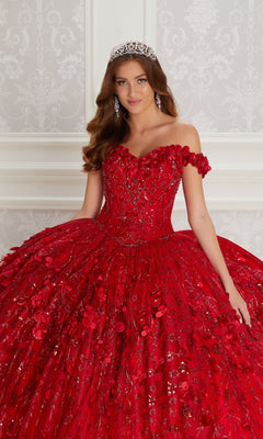 A young woman in the Flower Quince Dress: Princesa by Ariana Vara PR22036, a jeweled tiara, and an ornate red off-the-shoulder ball gown stands before a decorative white wall.