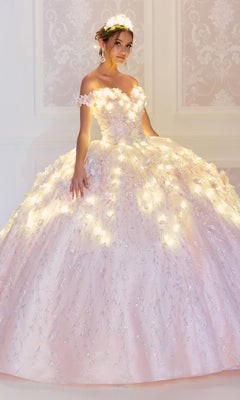 A young woman wears the Flower Quince Dress: Princesa by Ariana Vara PR22036, a light pink, off-the-shoulder ball gown with floral details and integrated lights, glowing softly as she stands against an ornate, light-colored wall.