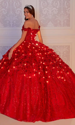 A young woman in the glow-in-the-dark Flower Quince Dress: Princesa by Ariana Vara PR22036, featuring embedded lights, a tiara, and earrings, stands before an ornate light-colored wall.
