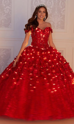 A young woman in the Flower Quince Dress: Princesa by Ariana Vara PR22036, a sparkling red ball gown, and a tiara stands before an ornate white wall.