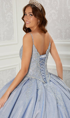 A young woman in the Quinceanera Dress PR22141 by Princesa, a light blue ball gown with a corset back and jeweled details, stands in an elegant white room wearing a tiara and looks over her shoulder.