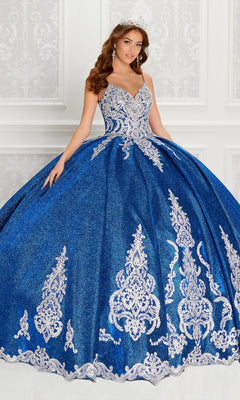 A woman in the Quinceanera Dress PR22141 by Princesa, a sparkling royal blue ball gown with silver embroidery and corset back, wears a tiara as she stands before an ornate white background.