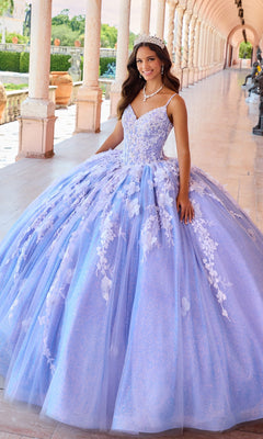 A young woman stands in a corridor wearing the Quinceanera Dress PR22143 By Princesa, featuring sparkling lavender fabric, floral details, a beaded corset bodice, and a tiara.