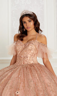 A young woman poses in front of a decorative white wall wearing the Quinceanera Dress PR22144 By Princesa, an ornate peach glitter gown with a corset back and a tiara.