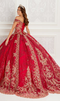 A woman wears the Quinceanera Dress PR22148 By Princesa, a red off-the-shoulder gown with gold lace embroidery and beaded accents, standing indoors against a white ornate wall and smiling over her shoulder.