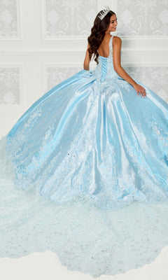 A young woman wearing the Quinceanera Dress PR30081 By Princesa—a sparkling light blue gown with delicate 3D flowers and a tiara—stands in an elegant room, facing away and glancing over her shoulder.