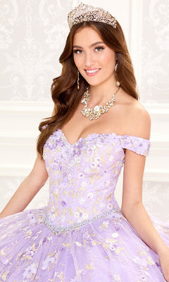 A young woman wearing a jeweled tiara, floral necklace, and the Quinceanera Dress PR30084 By Princesa with flower embroidery and a corset back poses and smiles in front of a patterned white background.