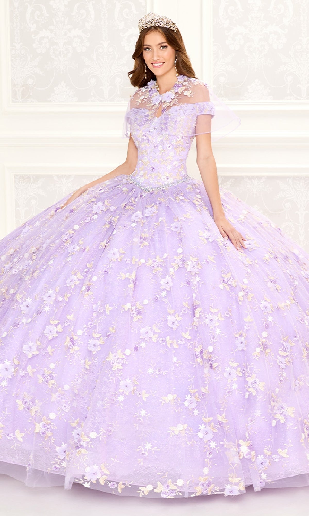 A woman poses in a formal setting wearing the Quinceanera Dress PR30084 By Princesa, featuring a lavender hue, corset back, and flower embellishments against a light decorative background.