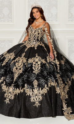 A woman stands smiling in front of a white patterned wall, wearing the Quinceanera Dress PR30085 By Princesa—black with gold embroidered lace, matching sheer cape, and a tiara on her head.