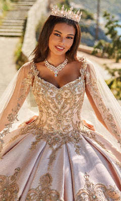 A woman in a jeweled crown and gold-embroidered Quinceanera Dress PR30085 By Princesa with metallic lace poses outdoors, smiling at the camera and wearing a necklace.