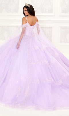 A woman in the Quinceanera Dress PR30087 By Princesa, featuring sparkling lavender fabric, off-the-shoulder sleeves, and a corset bodice with a tiara, stands before an ornate white wall, facing away but glancing over her shoulder.