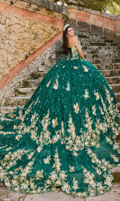 A woman in the Quinceanera Dress PR30111 by Princesa, a green gown with gold floral details and lace embroidery, stands on stone steps, smiling as she looks back over her shoulder.